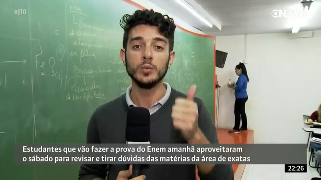 Jornalista gravando reportagem em sala de aula enquanto professora ministra aula ao fundo