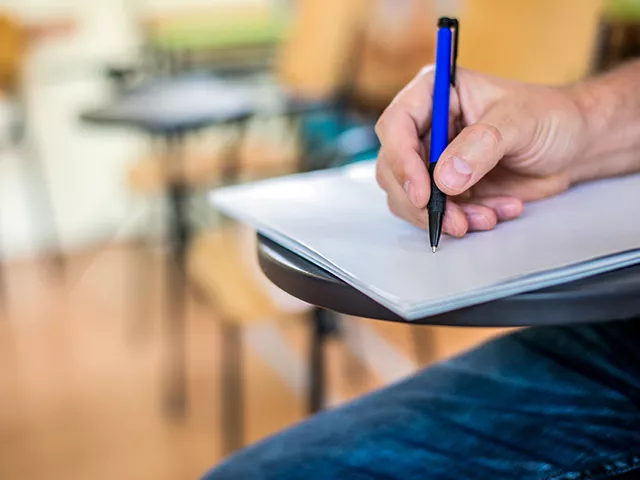 Aluno com caneta na mão escrevendo em um caderno